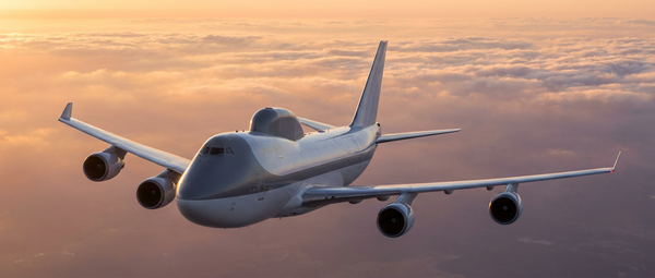 A strategic airborne operations center aircraft flying above high-altitude cloud cover during sunset.